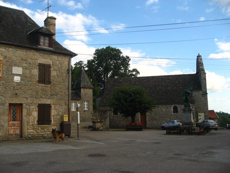 À gauche, le bureau de poste de Champagnac-la-Prune. Au milieu de la place, le monument aux morts. Derrière celui-ci, l'église, dans le département de la Corrèze.