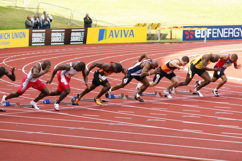 Des athlètes prennent le départ d'une course depuis leur starting-block. 